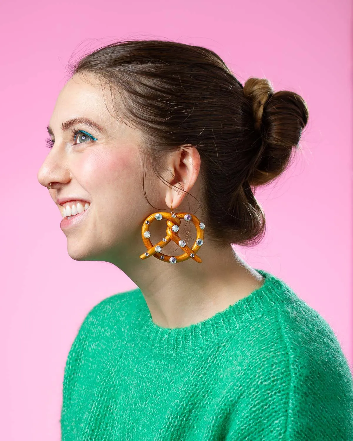 Headshot of Quinn Curnow wearing her own hand-made earrings on pink background